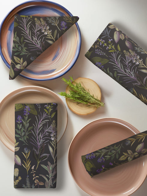 set of four dark charcoal cloth napkins with a repeating pattern of muted purple, green, and gold herbs and flowers in an elegant botanical design.